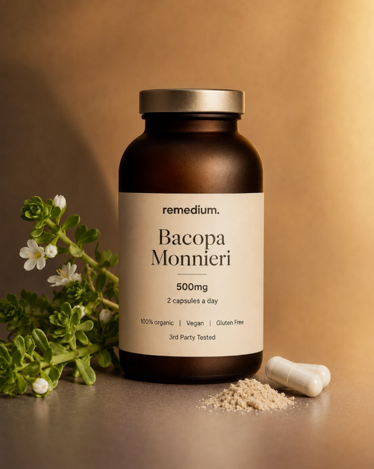 A bottle of Remedium Bacopa Monnieri dietary supplements, 500mg, with a silver cap and cream label, styled on a warm brown surface with green herbs and capsules.